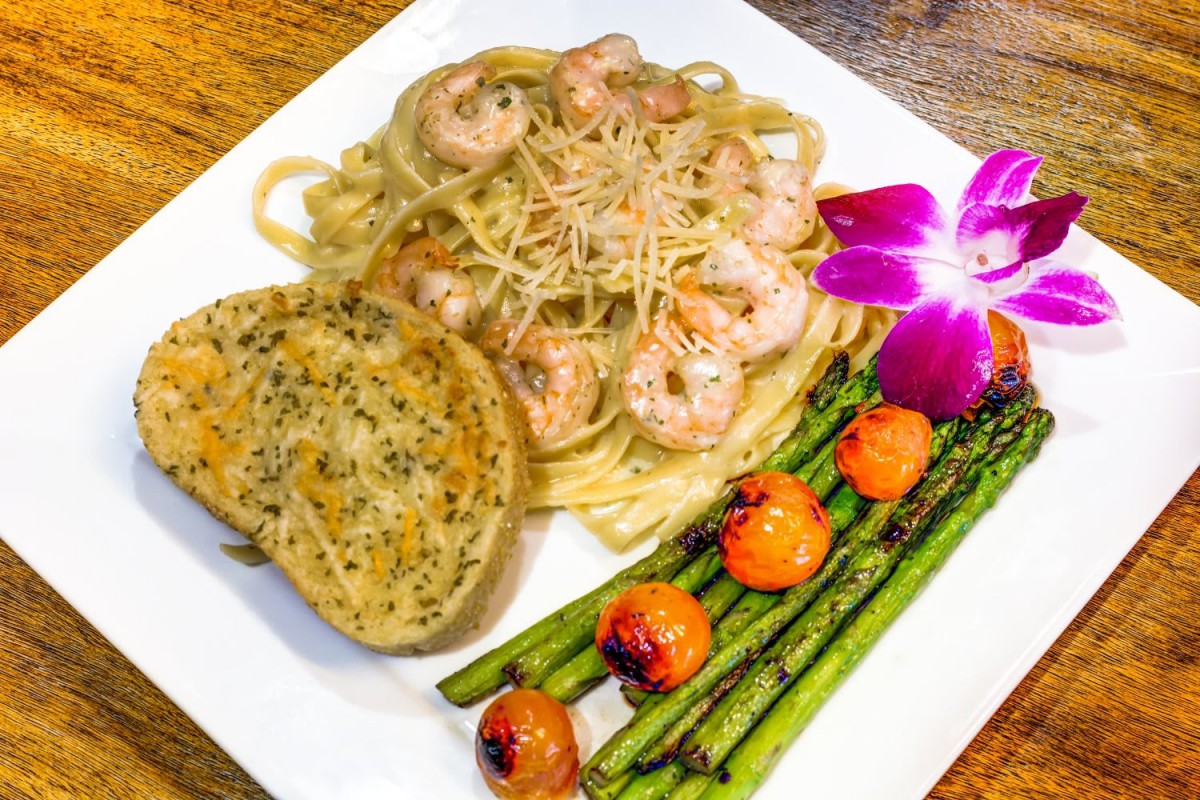 A gourmet shrimp pasta dish served with garlic bread, asparagus, and cherry tomatoes, garnished with a flower.