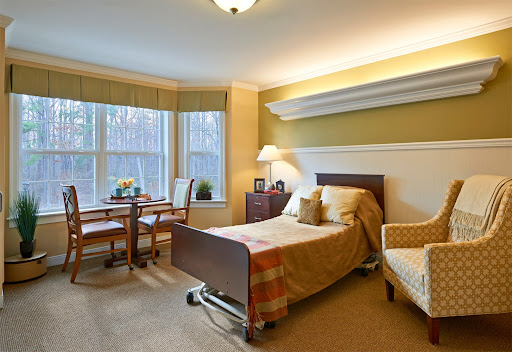 A well-lit hospital room featuring a bed, table, and chairs, designed for comfort and care.