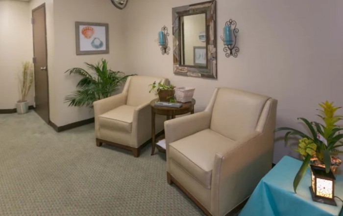 A cozy waiting room with two beige chairs, a small table, and decorative elements.