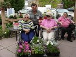 A group of people enjoying a day in the garden with plants and flowers around them.