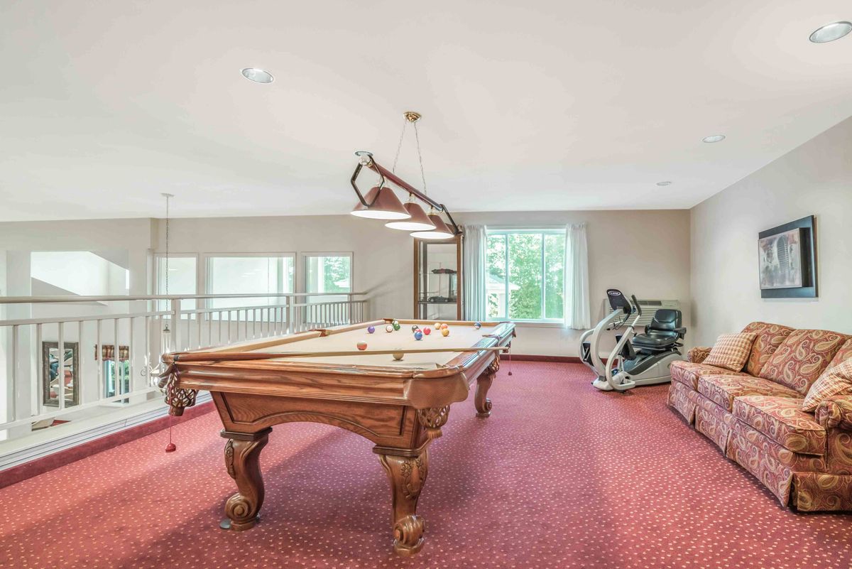 A spacious game room featuring a pool table and exercise equipment on a red carpeted floor.