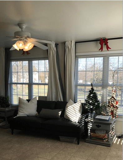 A cozy living room with a sofa, large windows, and festive Christmas decorations.