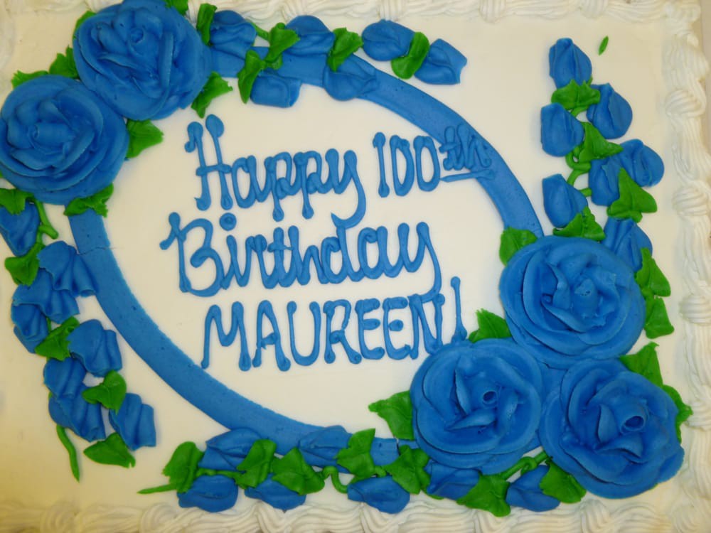 A beautifully decorated birthday cake with blue roses, celebrating Maureen's 100th birthday.