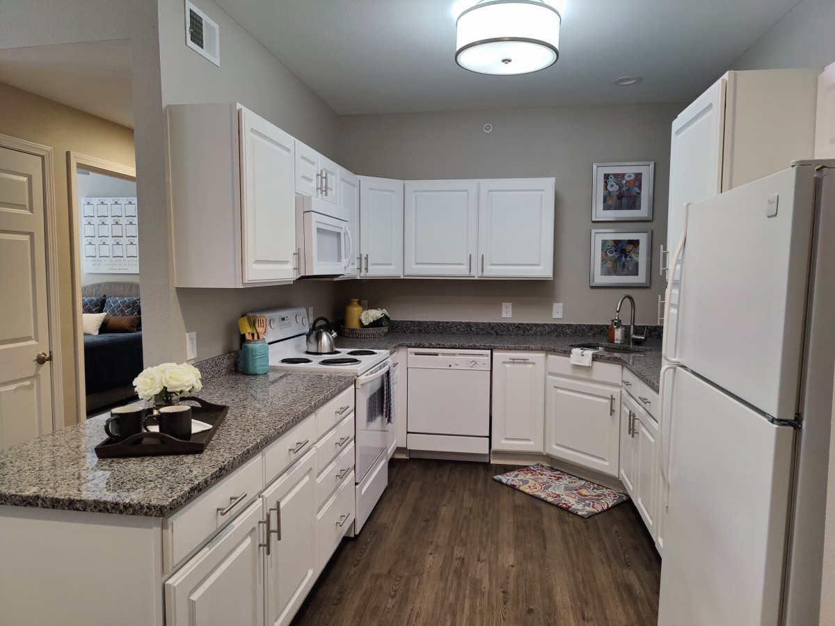 A modern kitchen with white cabinets and wooden flooring.