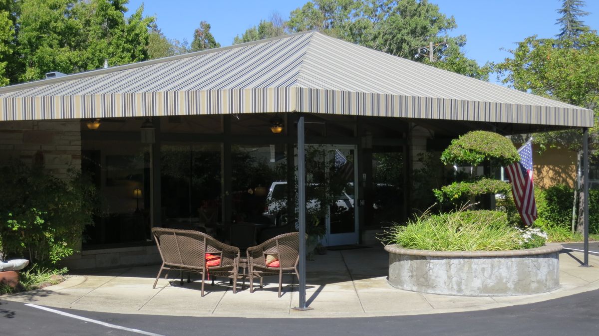 Outdoor seating area of a cafe with an awning and greenery.