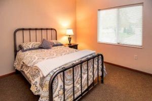 A cozy bedroom with a bed, nightstand, and lamp by the window.