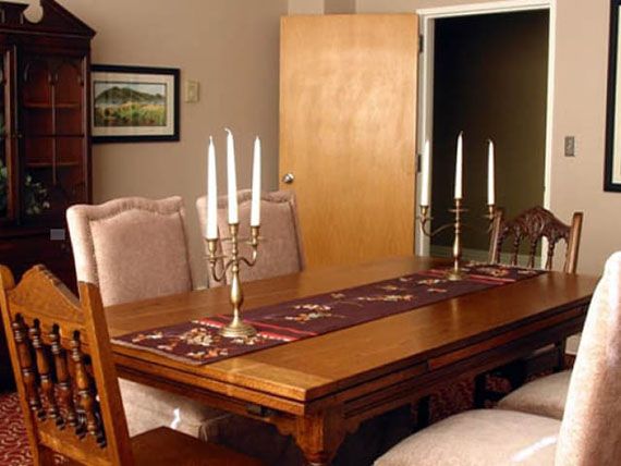A well-arranged dining room with a wooden table set for an elegant dinner, featuring multiple candles on a decorative runner.
