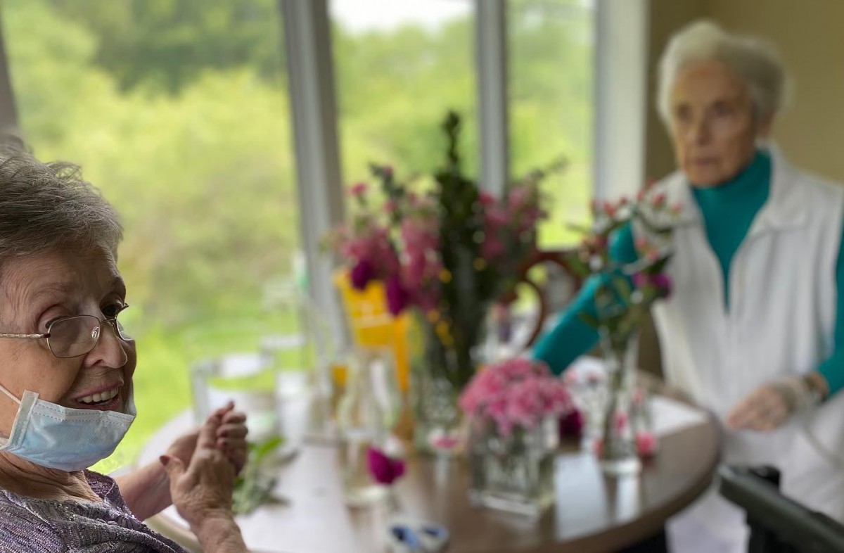 Two people engaged in conversation at a table adorned with flowers by a window.