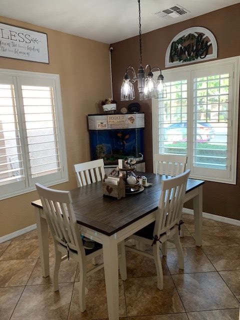 A cozy dining room with a wooden table and chairs, featuring stylish lighting and window shutters.