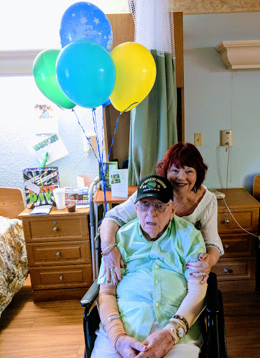 A heartwarming moment of celebration with an elderly person and their caregiver, surrounded by colorful balloons.