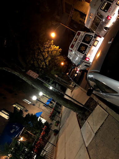 A nighttime view of a city street with parked cars and ambient lighting.