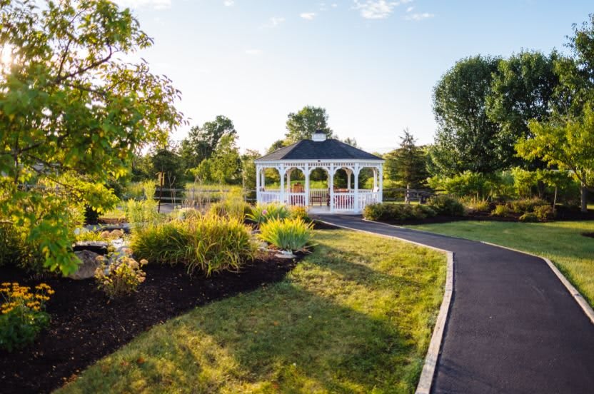 A tranquil garden scene featuring a white gazebo surrounded by lush greenery and a winding pathway.
