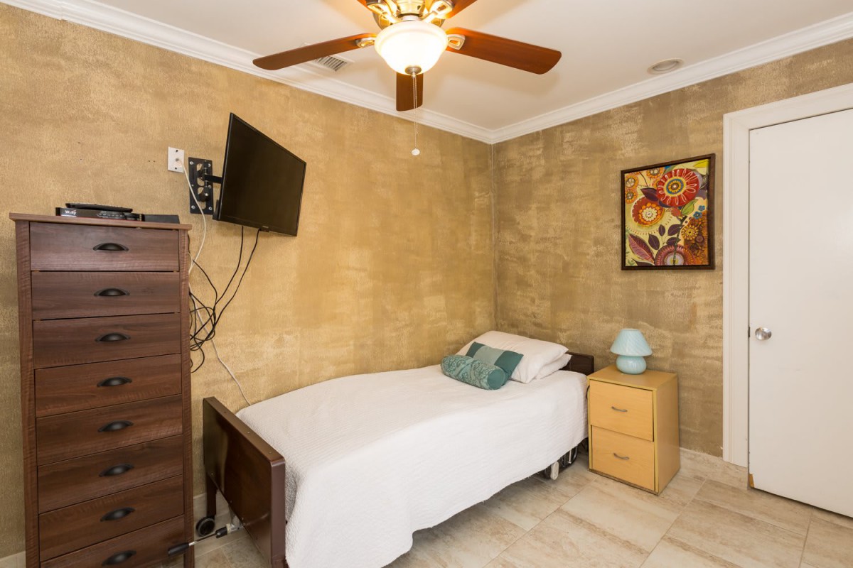 A cozy bedroom with a single bed, wall-mounted TV, and a ceiling fan.