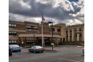 A hospital building with parked cars and a cloudy sky in the background.