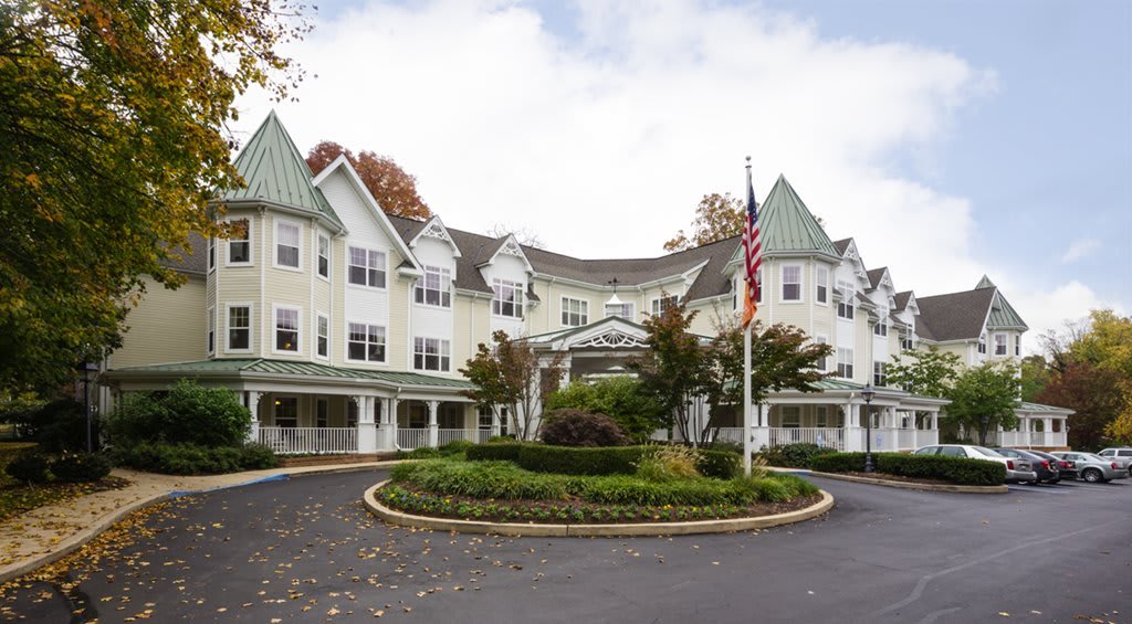 A large, multi-story building with decorative architecture and a well-maintained garden in the foreground, featuring an American flag on a pole.