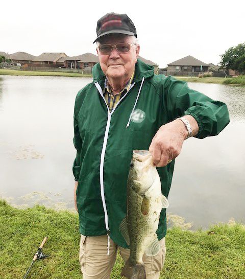 A person proudly holding a fish by the lake.