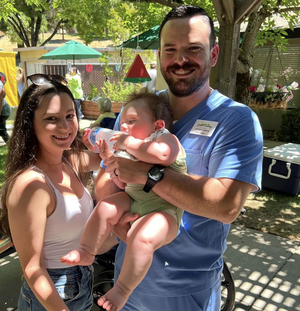 A family enjoying a sunny day outdoors, with parents holding their baby and smiling.