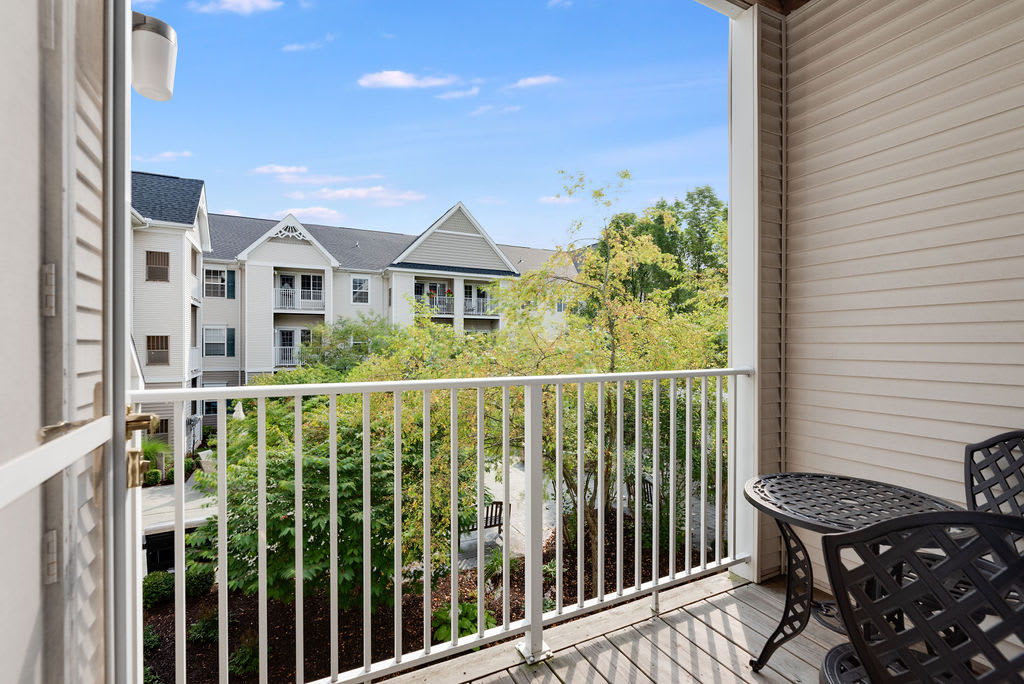 A balcony with a view of a residential apartment complex, featuring outdoor furniture and surrounded by greenery.