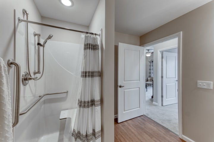 A bathroom with a shower featuring a striped curtain, and an open doorway leading to a hallway.