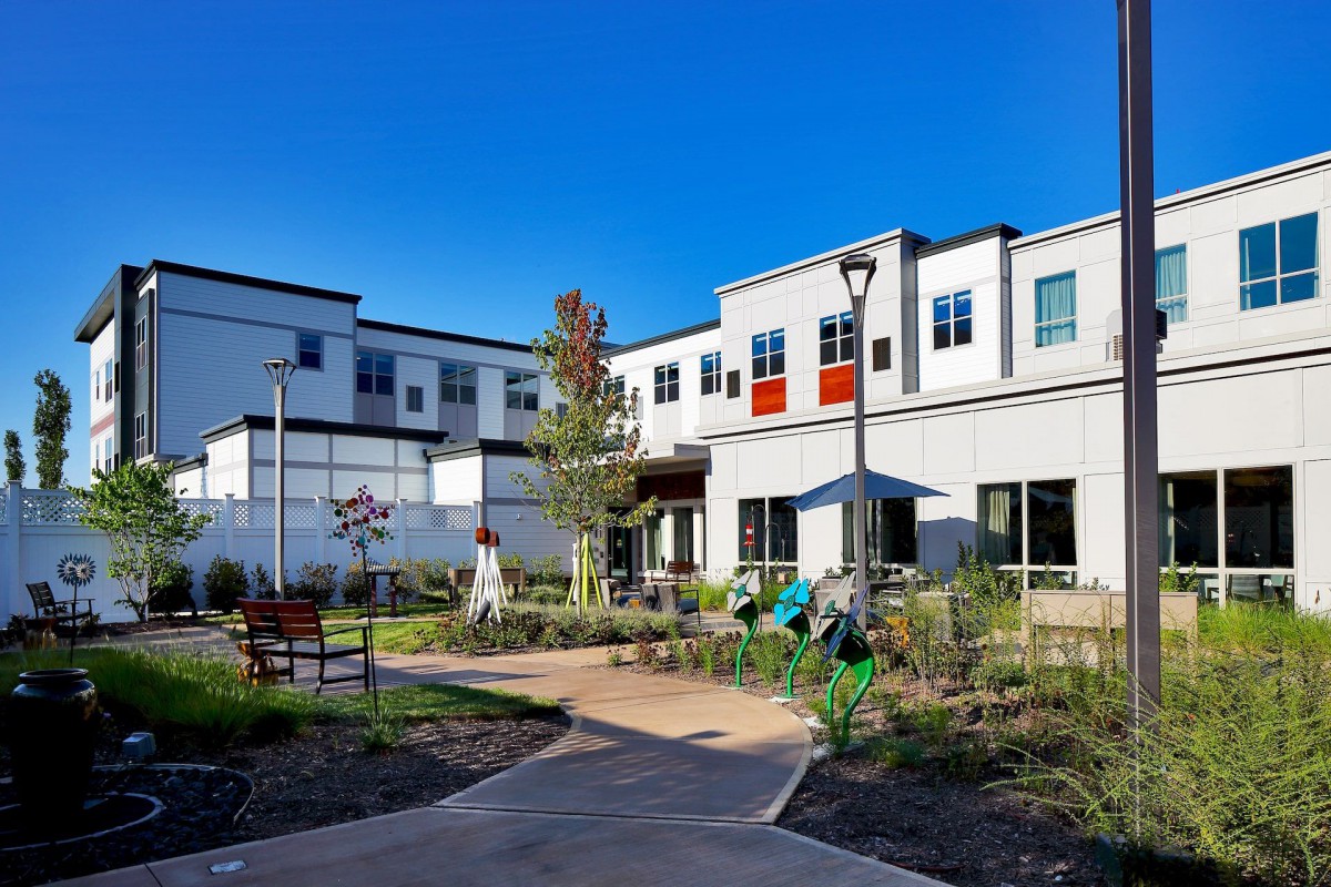 A modern residential building with a landscaped garden and pathway on a sunny day.