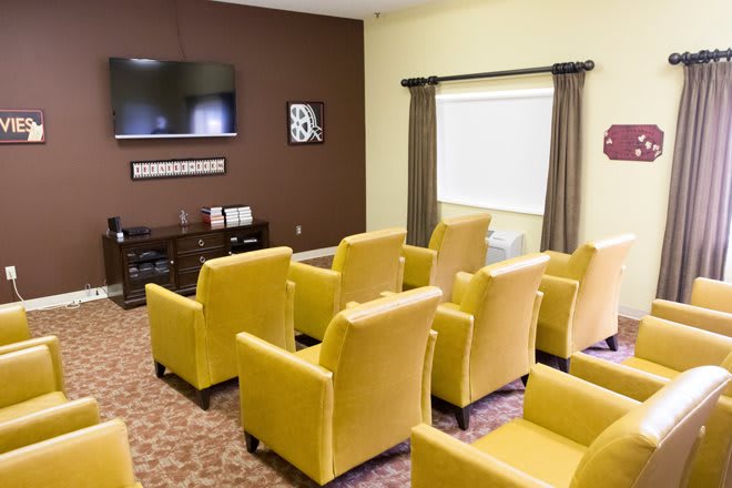 A neatly arranged room with yellow armchairs facing a mounted television.