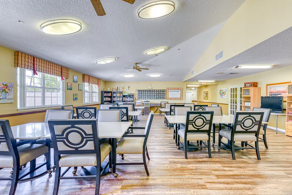 A spacious dining area with neatly arranged tables and chairs, featuring wooden flooring and ceiling fans.