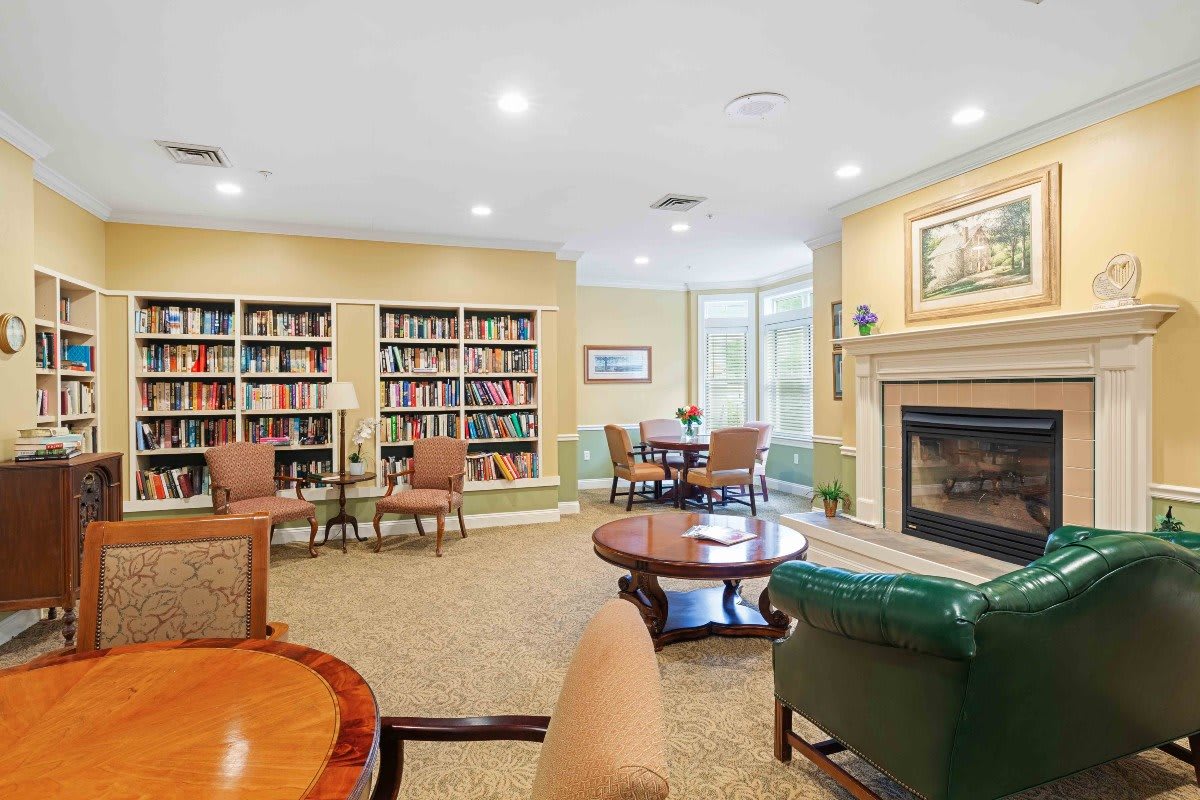 A cozy reading room with bookshelves and a fireplace, featuring comfortable seating.