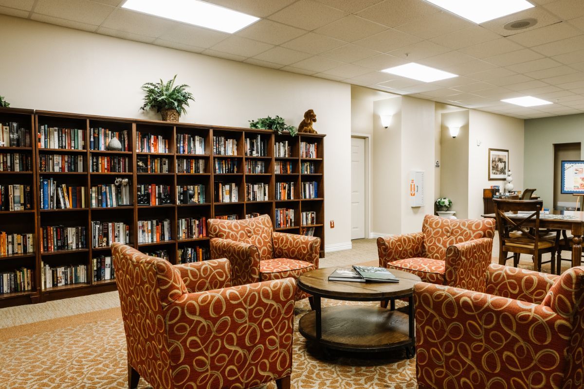 A cozy reading area with a bookshelf, featuring comfortable chairs and a round table.