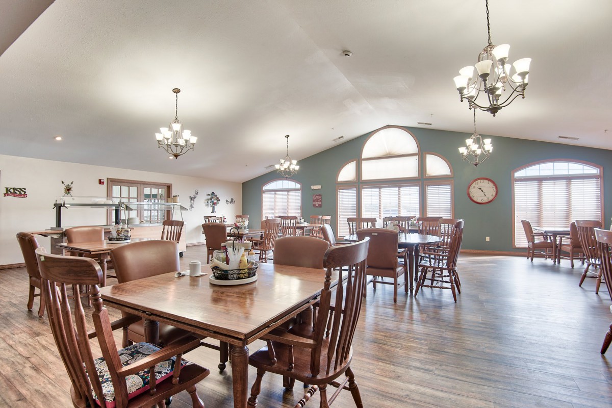 A spacious dining room featuring wooden furniture, large windows, and elegant chandeliers.