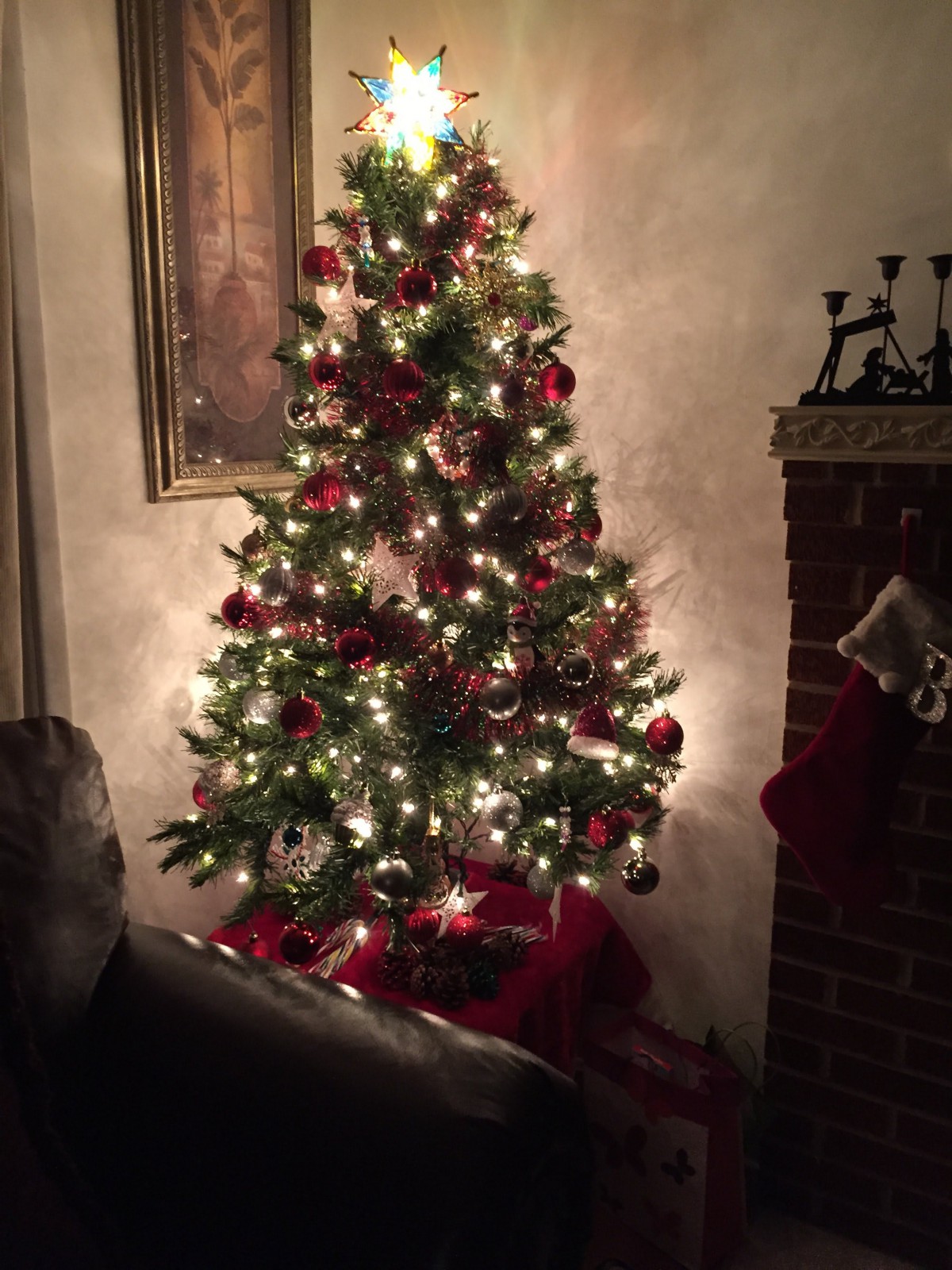 A beautifully decorated Christmas tree with lights and ornaments beside a fireplace.