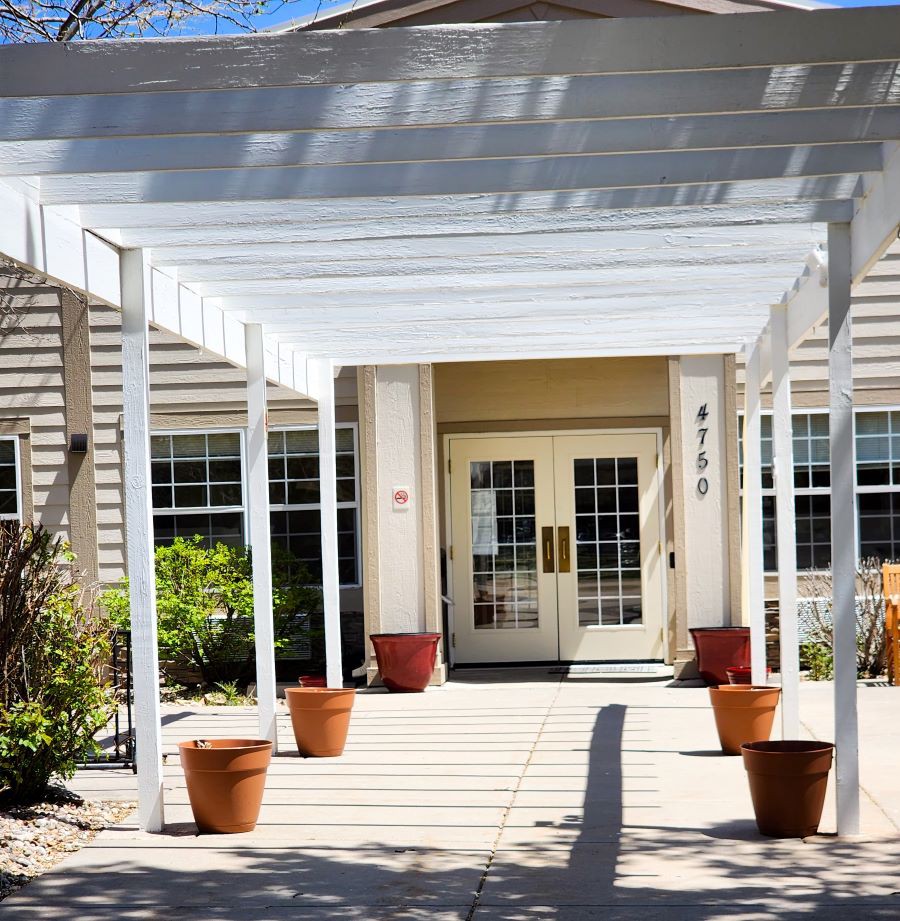 A building entrance with a white pergola and potted plants.