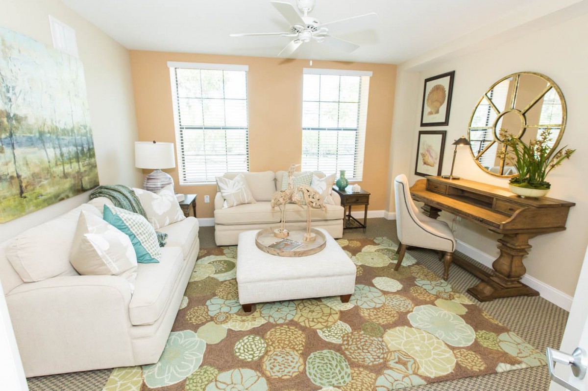 A cozy living room featuring a comfortable sofa, an armchair, and a stylish rug with soft lighting from two large windows.