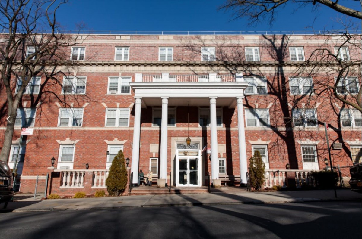 A large brick building with white columns at the entrance, set against a clear blue sky.