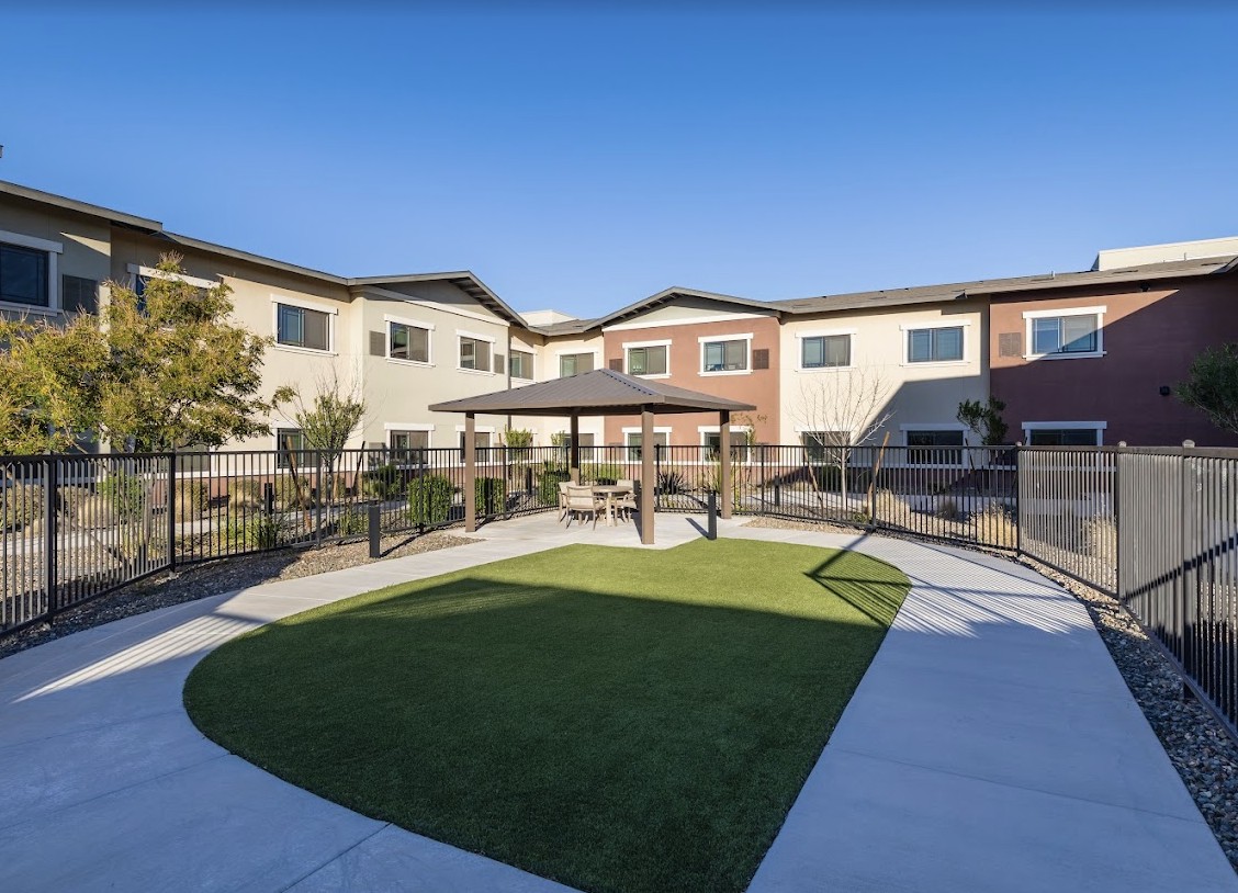 A modern residential building with a fenced courtyard featuring a grassy area.