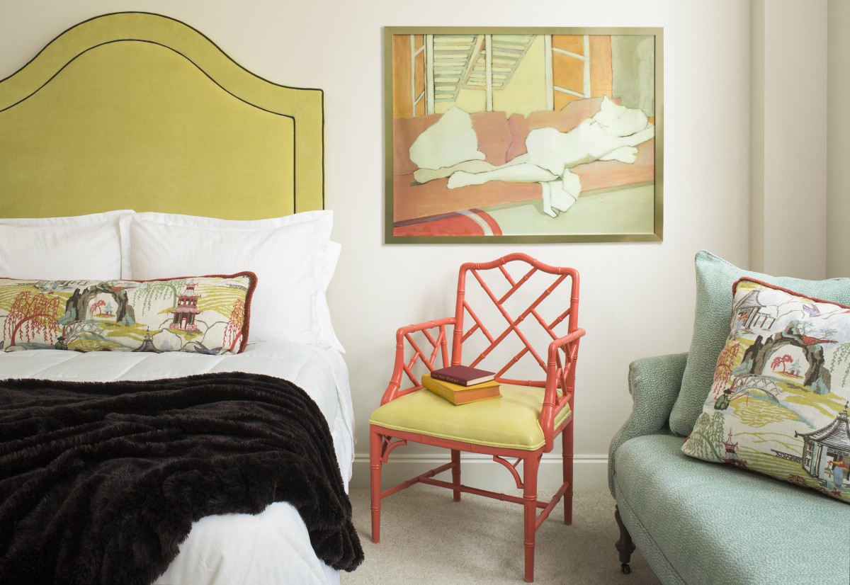 A stylish bedroom featuring a unique red chair, an abstract painting on the wall, and a cozy bed with plush pillows.