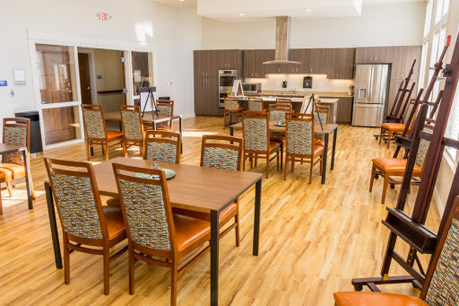 A spacious and modern dining area featuring wooden tables and chairs, with a well-equipped kitchen in the background.