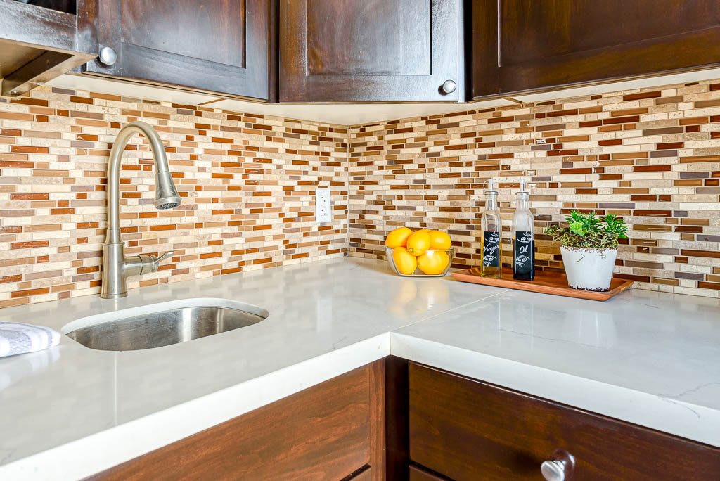 Modern kitchen corner with mosaic backsplash and stainless steel sink.