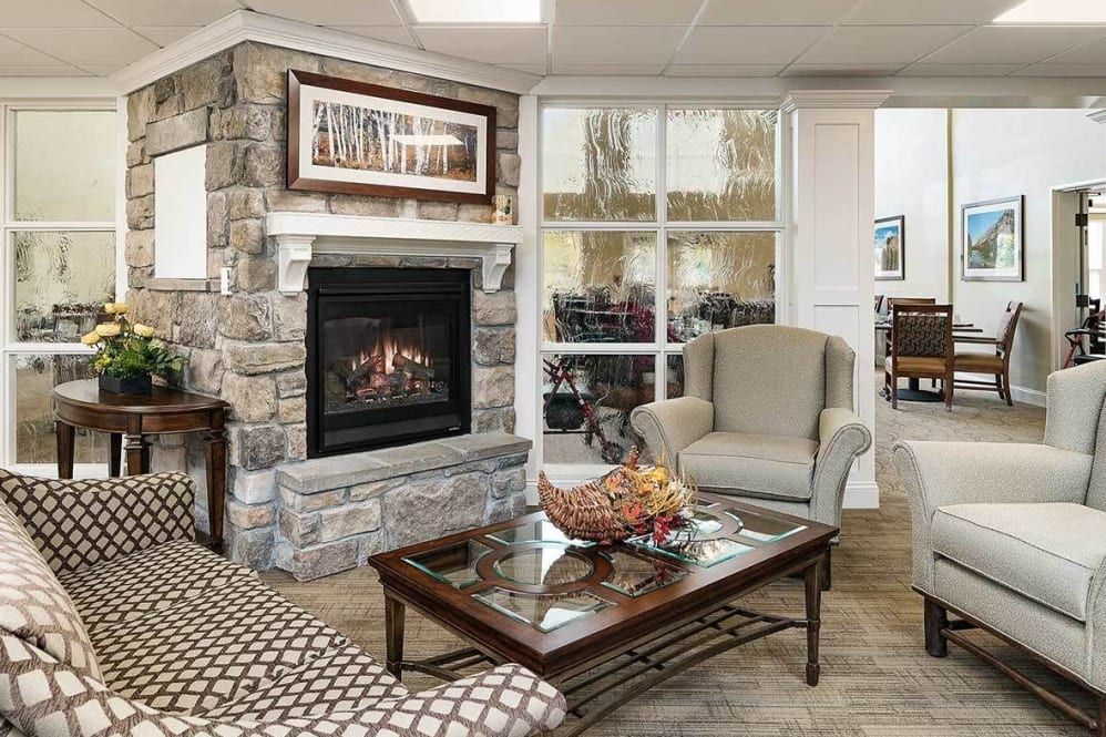 A cozy living room with a stone fireplace, armchair, and a glass coffee table adorned with decorative objects.