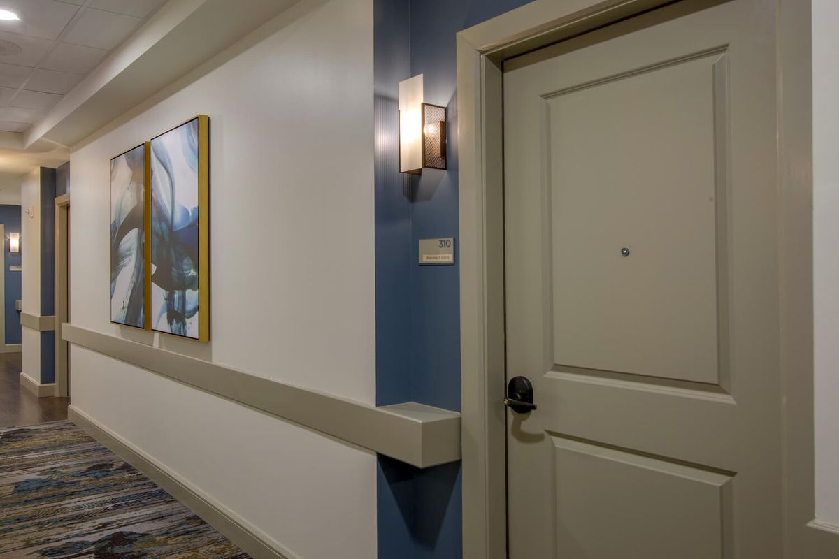 A hotel hallway featuring a door, wall light, and painting.