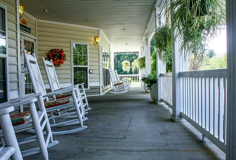 A cozy porch with rocking chairs and greenery, inviting relaxation in a sunny setting.