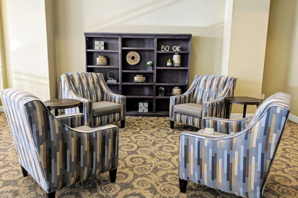 A cozy lounge area featuring patterned armchairs and a bookshelf adorned with decorative items.