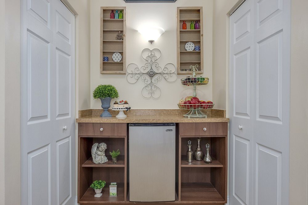 A well-organized kitchen nook featuring a small refrigerator, wooden shelving with decorative items, and wall-mounted cabinets.