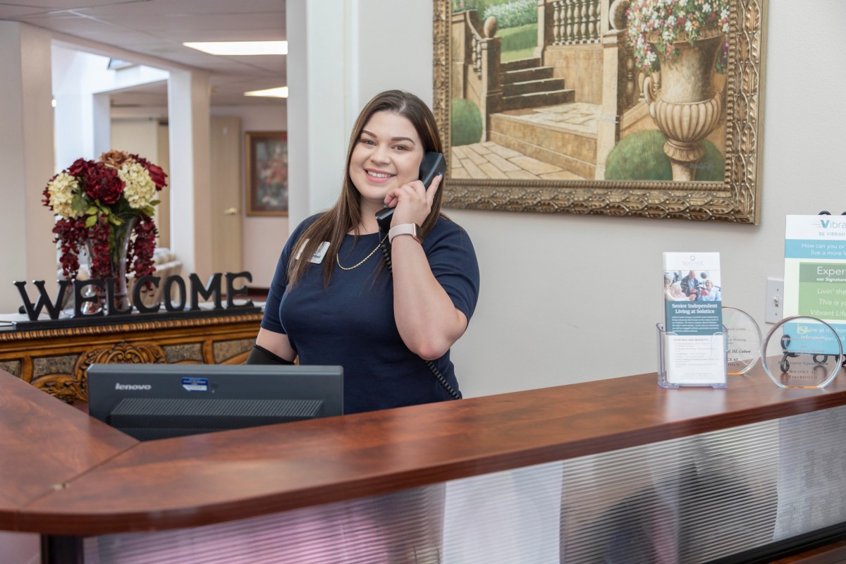 A receptionist smiling while talking on the phone at an office desk.