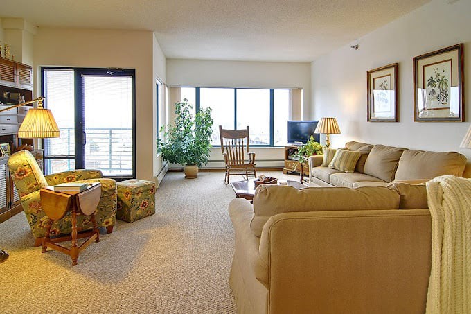 A cozy living room with a beige sofa, rocking chair, and large windows providing natural light.