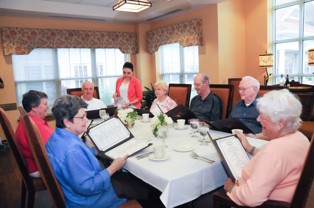A group of senior citizens enjoying a meal together at a restaurant, browsing menus and engaging in lively conversation.
