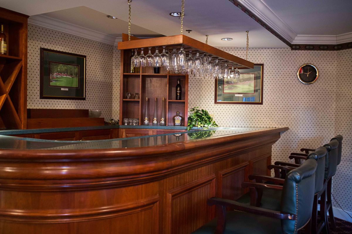An empty bar with a wooden counter and glasses hanging, creating a cozy atmosphere.