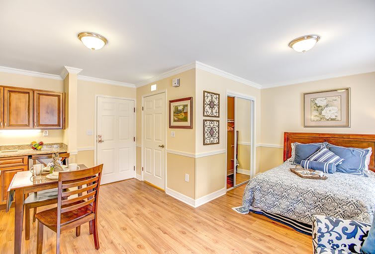 A cozy bedroom interior with wooden flooring, featuring a bed, desk, and chair.