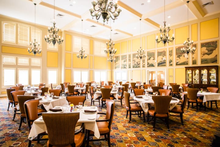 An elegant restaurant dining room with neatly set tables and chandeliers.