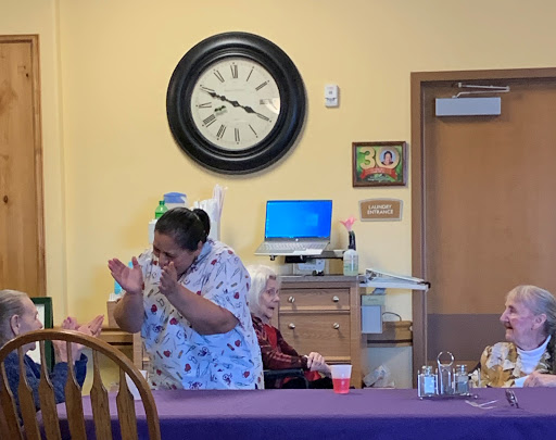 A caregiver engages with an elderly resident in a lively moment at a community center.