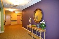 A hallway with a purple accent wall featuring a decorative table, mirror, and floral arrangement.